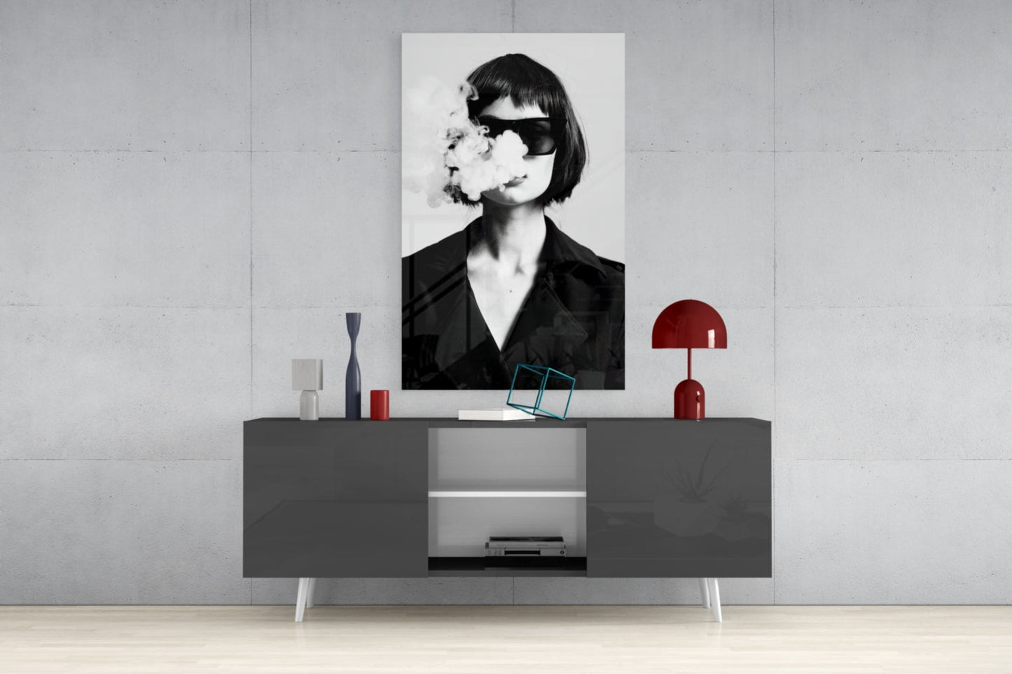 Black and white portrait of woman wearing sunglasses and black shirt, displayed on wall above gray console table with red lamp and decorative objects.