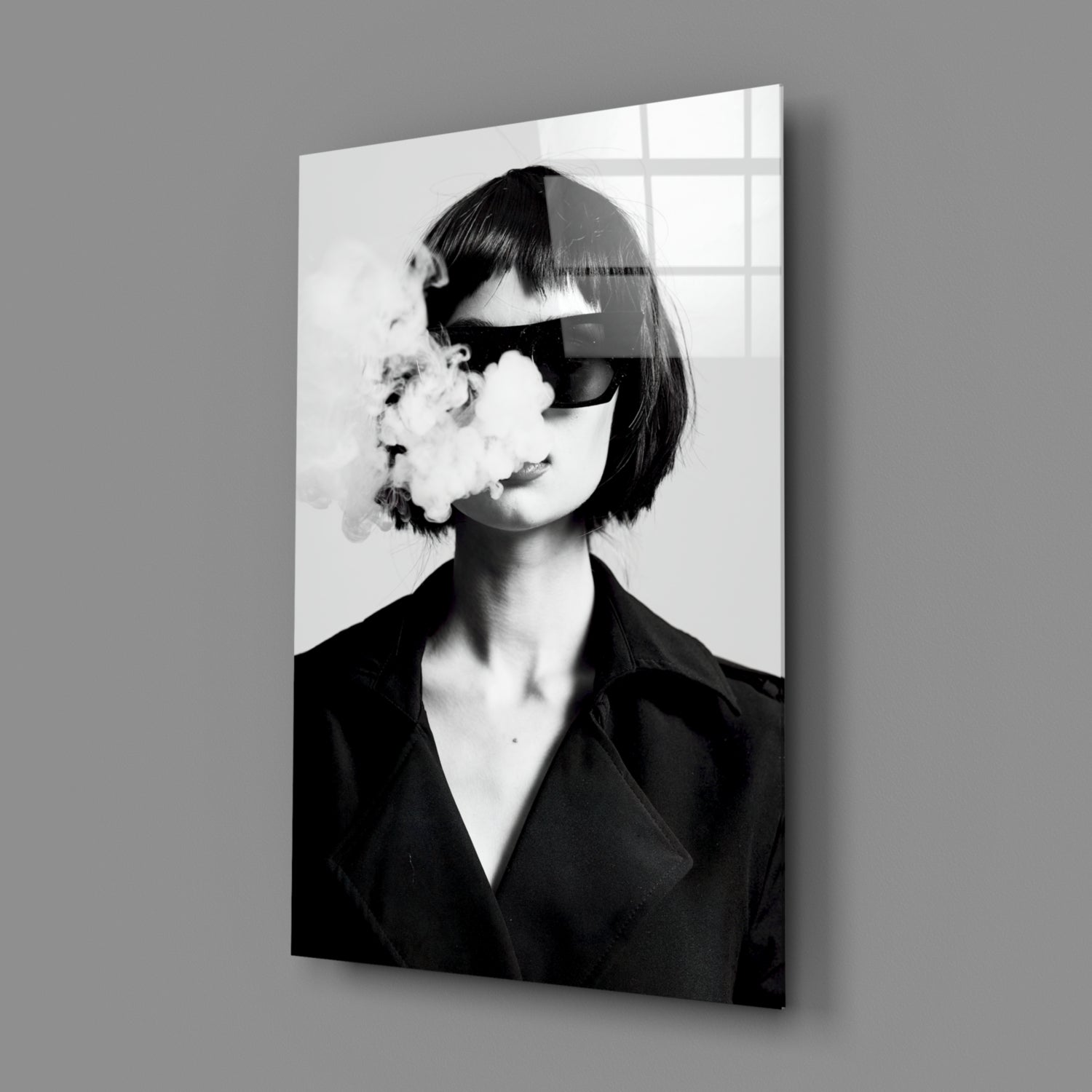 Black and white glass wall art showing a woman in sunglasses and dark blazer exhaling smoke, displayed at an angle against gray wall.
