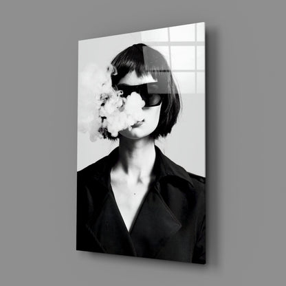 Black and white glass wall art showing a woman in sunglasses and dark blazer exhaling smoke, displayed at an angle against gray wall.