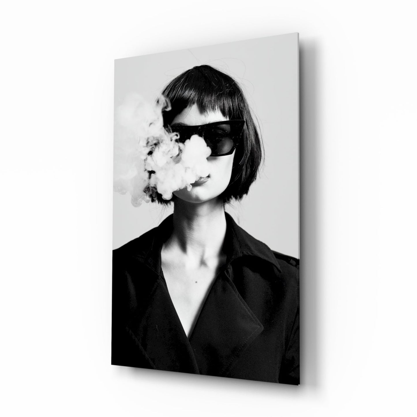 Black and white portrait of woman wearing dark blazer and oversized sunglasses, exhaling smoke, mounted on glass wall art panel.