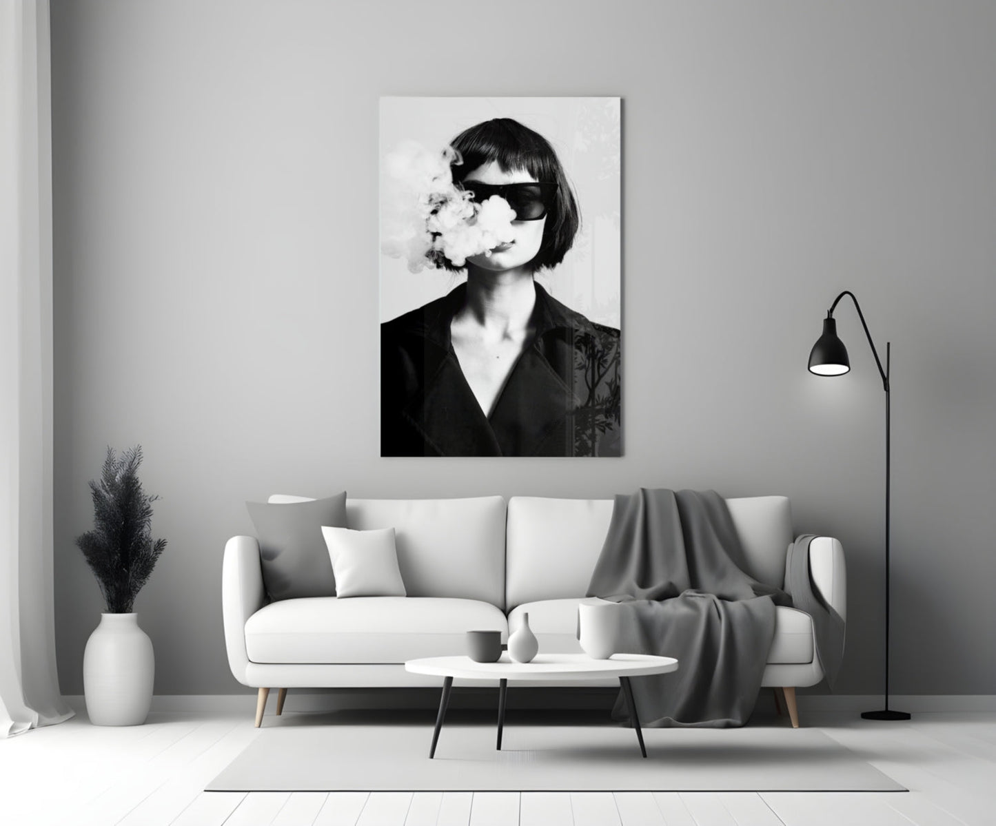 Black and white portrait of woman wearing sunglasses exhaling smoke, displayed as framed wall art above living room sofa.