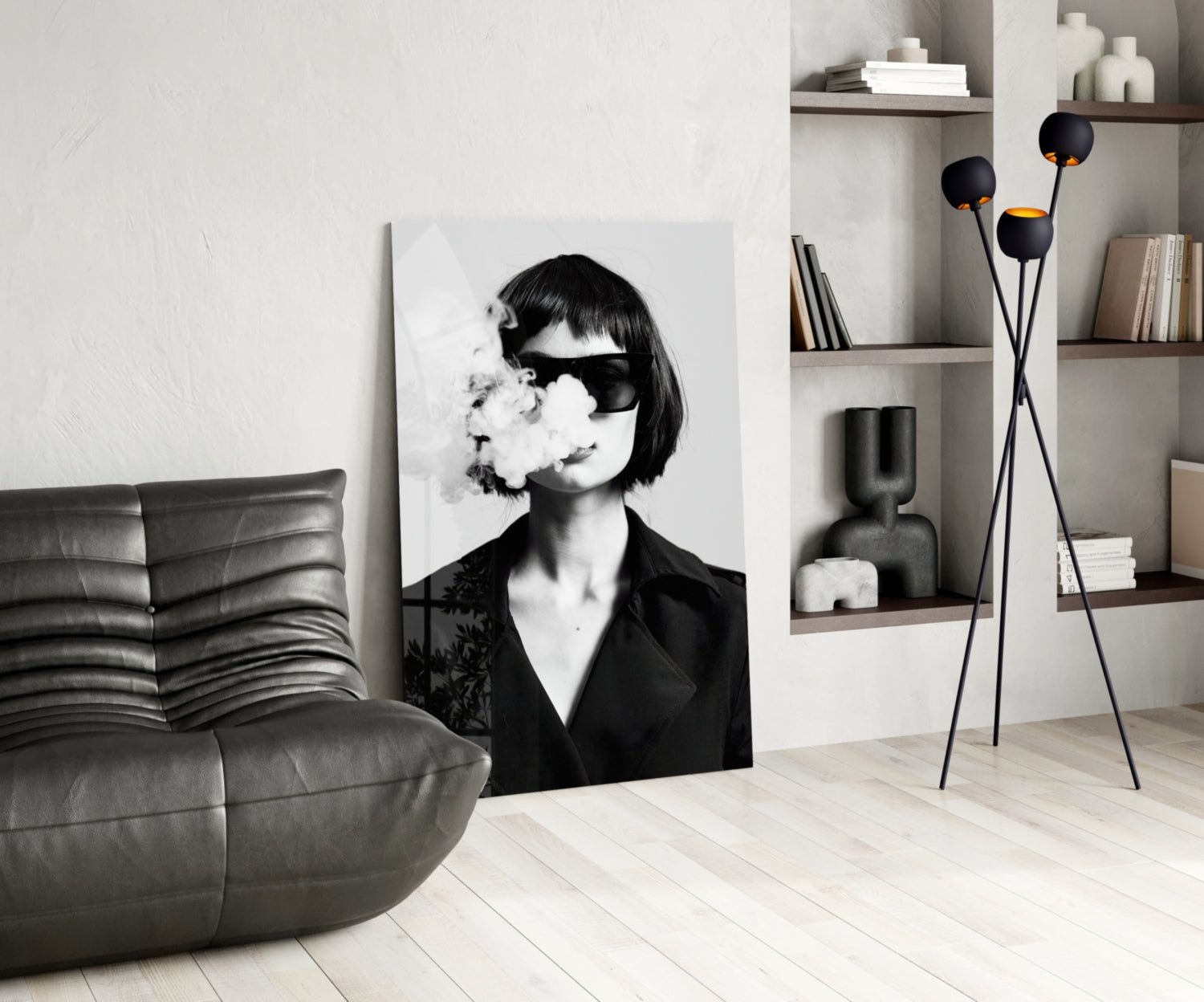 Modern living room interior featuring a black and white portrait glass wall art of a woman wearing sunglasses and exhaling smoke, displayed next to a gray leather chair and decorative shelving.