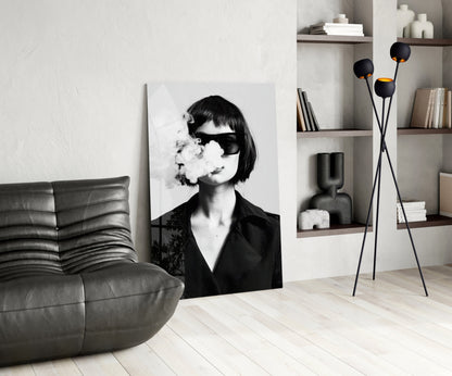 Modern living room interior featuring a black and white portrait glass wall art of a woman wearing sunglasses and exhaling smoke, displayed next to a gray leather chair and decorative shelving.