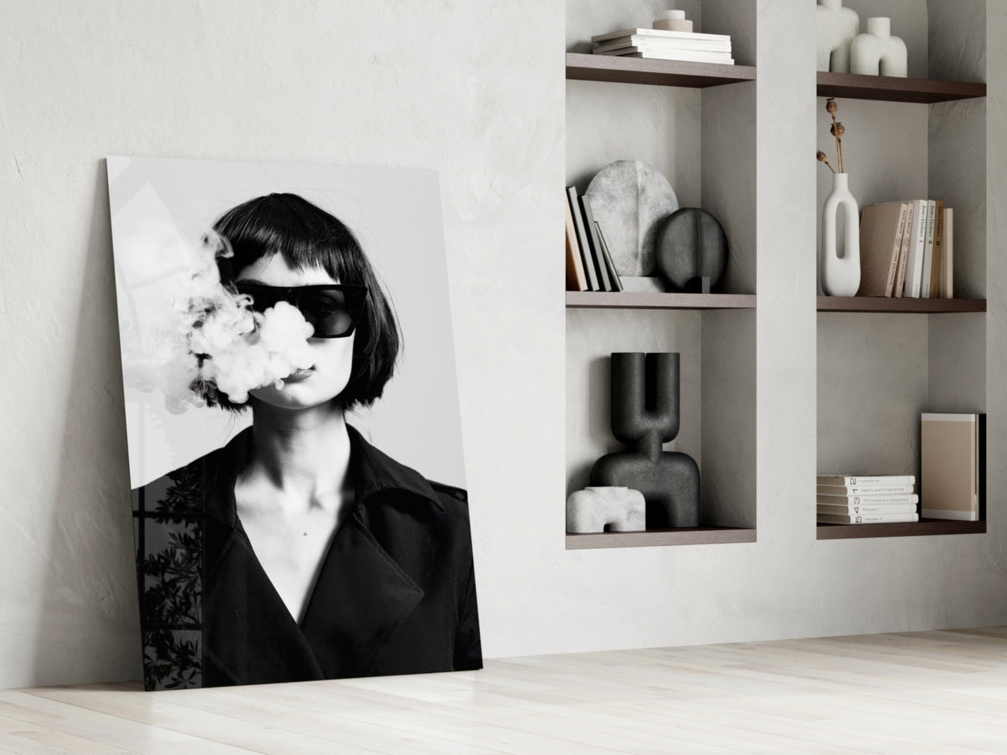 Black and white glass art leaning against white wall showing woman in sunglasses exhaling smoke, displayed in minimalist interior setting.