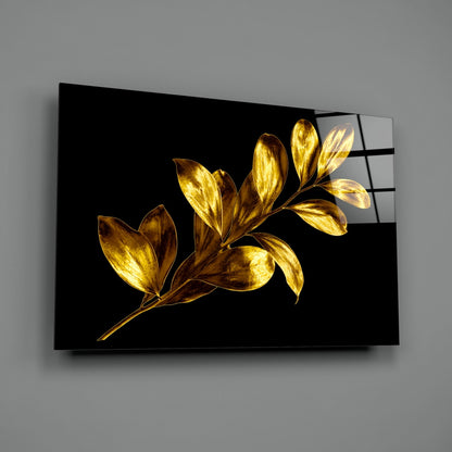 Black glass wall art panel displaying gold-leafed botanical branches against dark background, mounted at angle on gray wall.