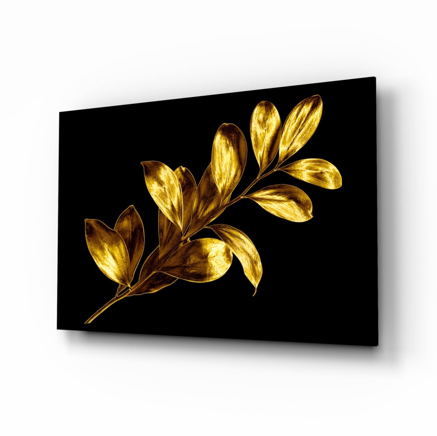 Angled perspective of gold-leafed botanical glass wall art displaying a branch with oval leaves against a black background.