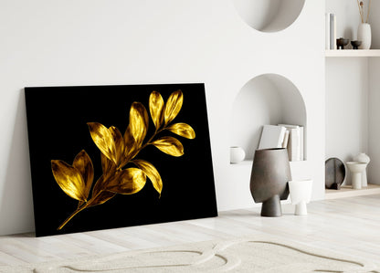 Yellow and gold leaves on black glass art leaning against white wall in minimalist interior setting.