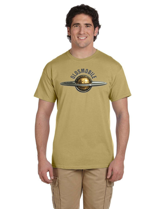 Front view of a smiling man in a sand-colored tee with a chrome globe emblem and arched OLDSMOBILE lettering.