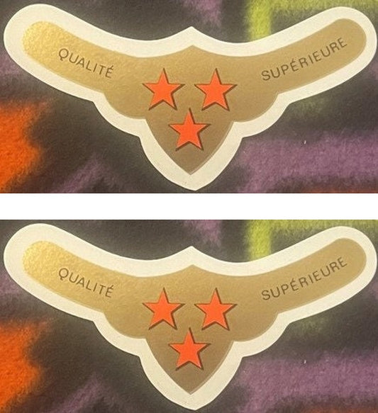 Two QUALITÉ SUPÉRIEURE neck labels, one above the other: three red stars, two over one, on a gold spread-wing ground inside a cream border