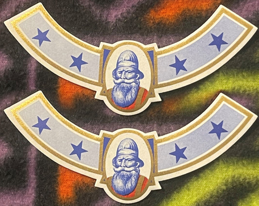 Two antique Viking neck labels, one above the other on a colorful fleece: a bearded Norseman in a tall blue cap in a gold-framed oval, blue stars on curved grey-blue arms, gold rules.
