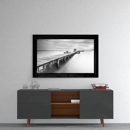 Black and white glass wall art of wooden pier in calm water