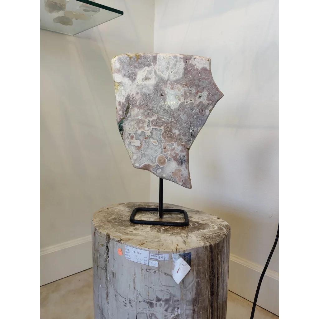 Pink amethyst polished slab sculpture with gray white green brown swirls on metal display stand and fossilized log base