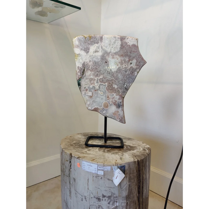 Pink amethyst polished slab sculpture with gray white green brown swirls on metal display stand and fossilized log base