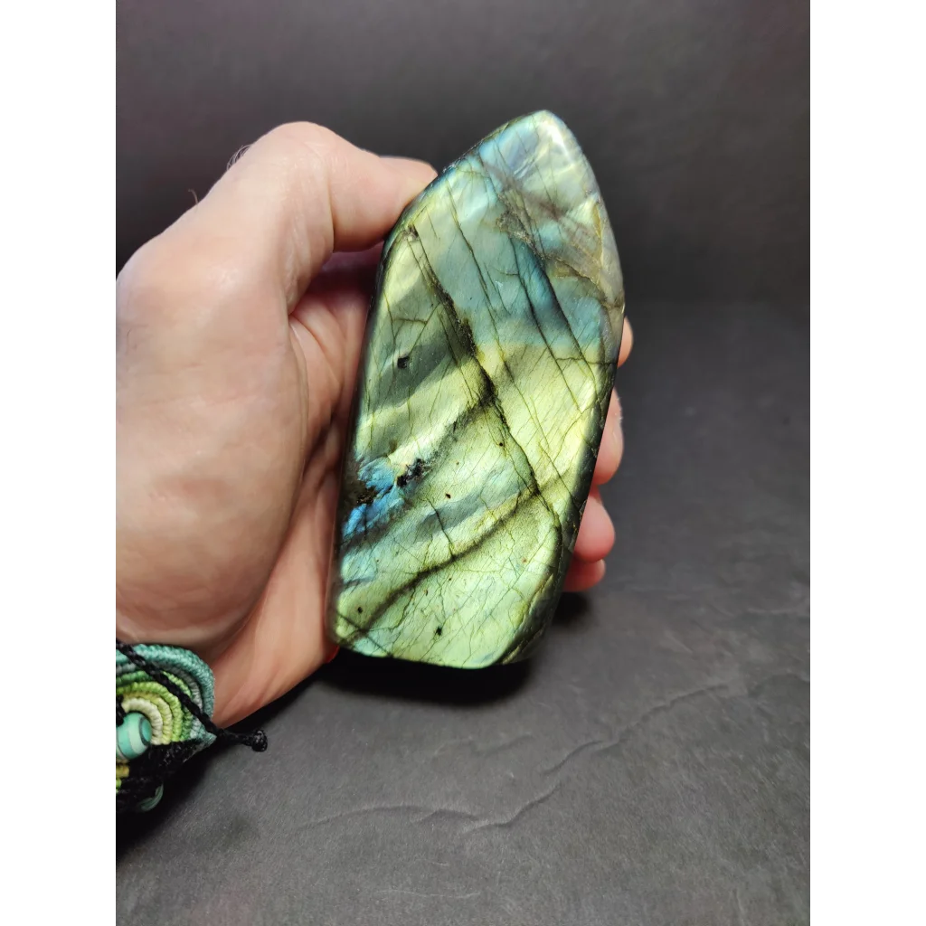 Polished labradorite free form sculpture with vibrant green and blue iridescence on a translucent base
