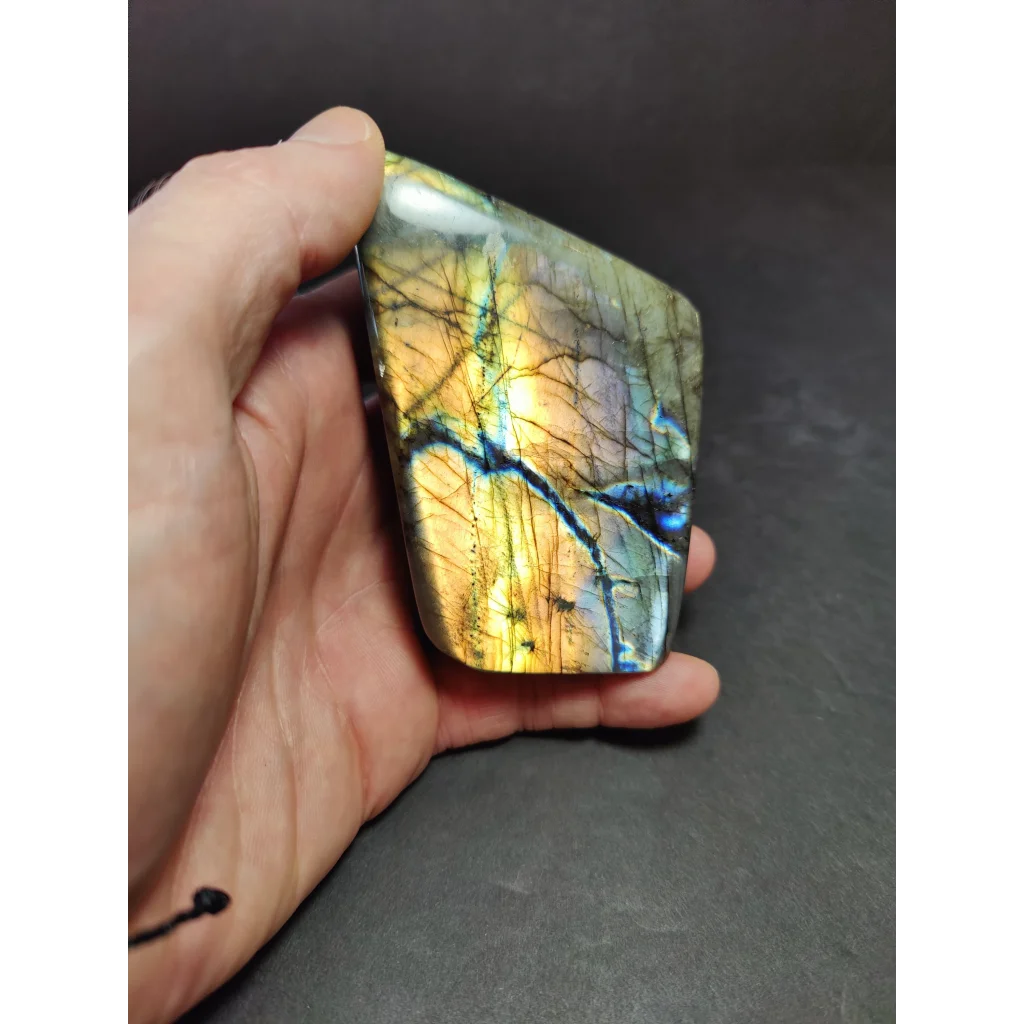 A hand holds a polished labradorite free form sculpture with vibrant golden yellow and deep blue iridescent patterns