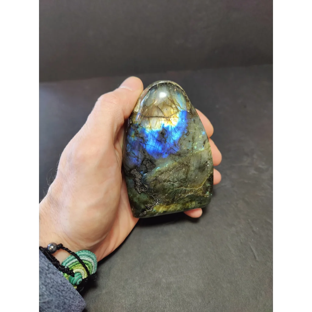 Polished labradorite free form sculpture featuring a teardrop shape with iridescent blue and gold hues on dark green base