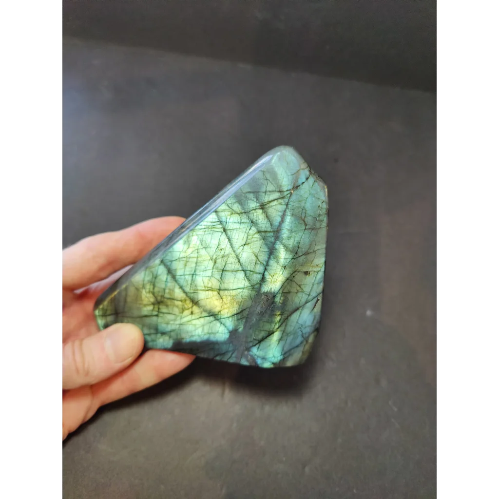Polished labradorite free form sculpture featuring a triangular stone with shimmering green and blue iridescent hues