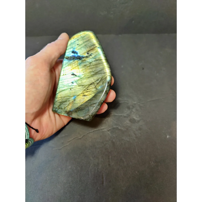 A hand holds a polished labradorite free form sculpture with iridescent green and blue flashes