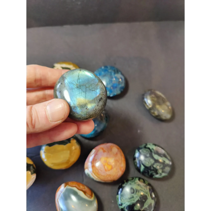 A hand holds a polished palmstone labradorite with iridescent blue and green hues shimmering under light