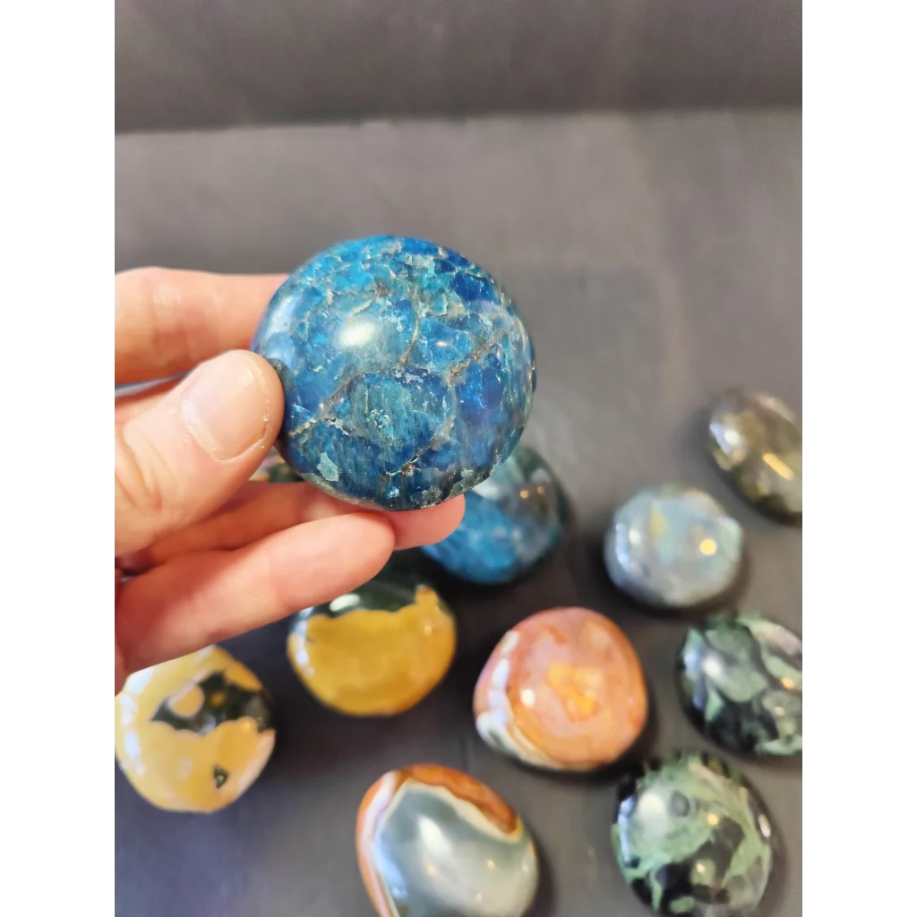 A hand holds a polished blue agate palmstone sphere with intricate crackled patterns and natural mineral inclusions