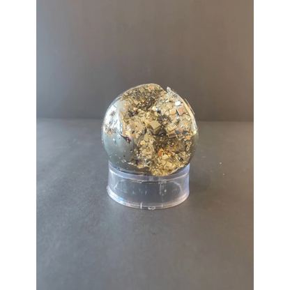 A polished pyrite geode with a golden reflective crystalline surface displayed on a clear acrylic stand