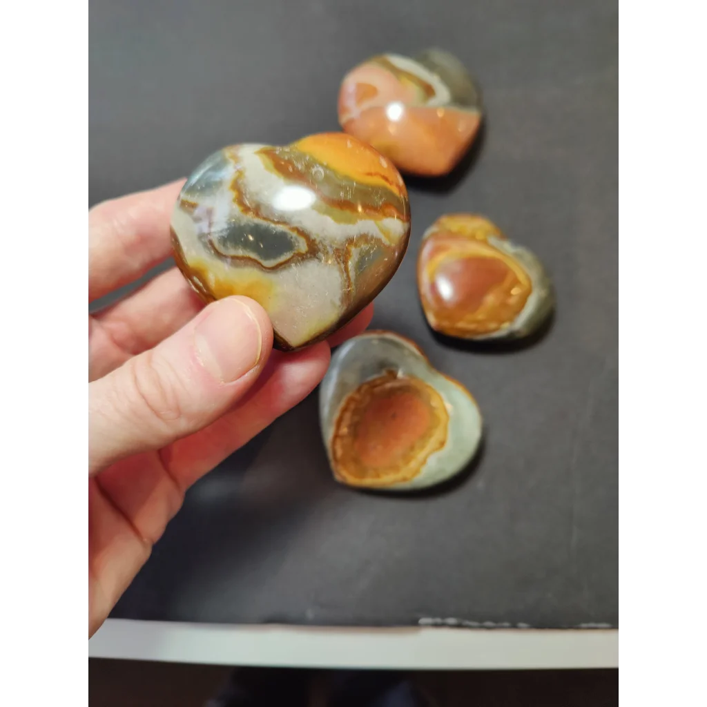 Hand holding a polished polychrome jasper carved heart stone with orange and white banded patterns