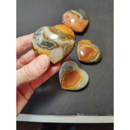 Hand holding a polished polychrome jasper carved heart stone with orange and white banded patterns
