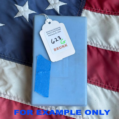 Light blue rectangular plastic case with white tag and blue tape containing president jimmy carter’s fly fishing lure
