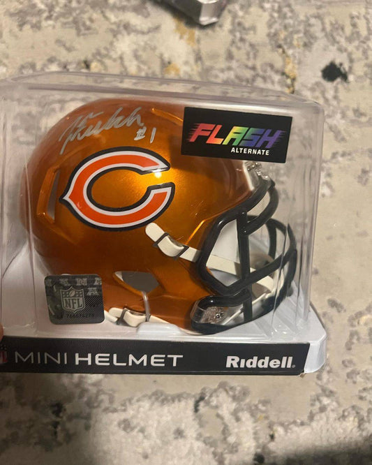 Autographed Chicago Bears orange mini helmet in clear plastic packaging with "Flash Alternate" label visible, displayed on concrete surface.