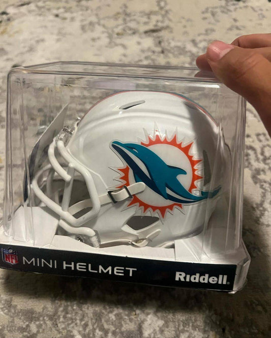 White Riddell mini helmet with teal dolphin and orange sunburst logo displayed in clear plastic case packaging.