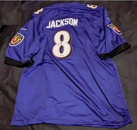 Back view of a purple football jersey on dark fabric, showing the white JACKSON name, number 8, and black sleeve trim.