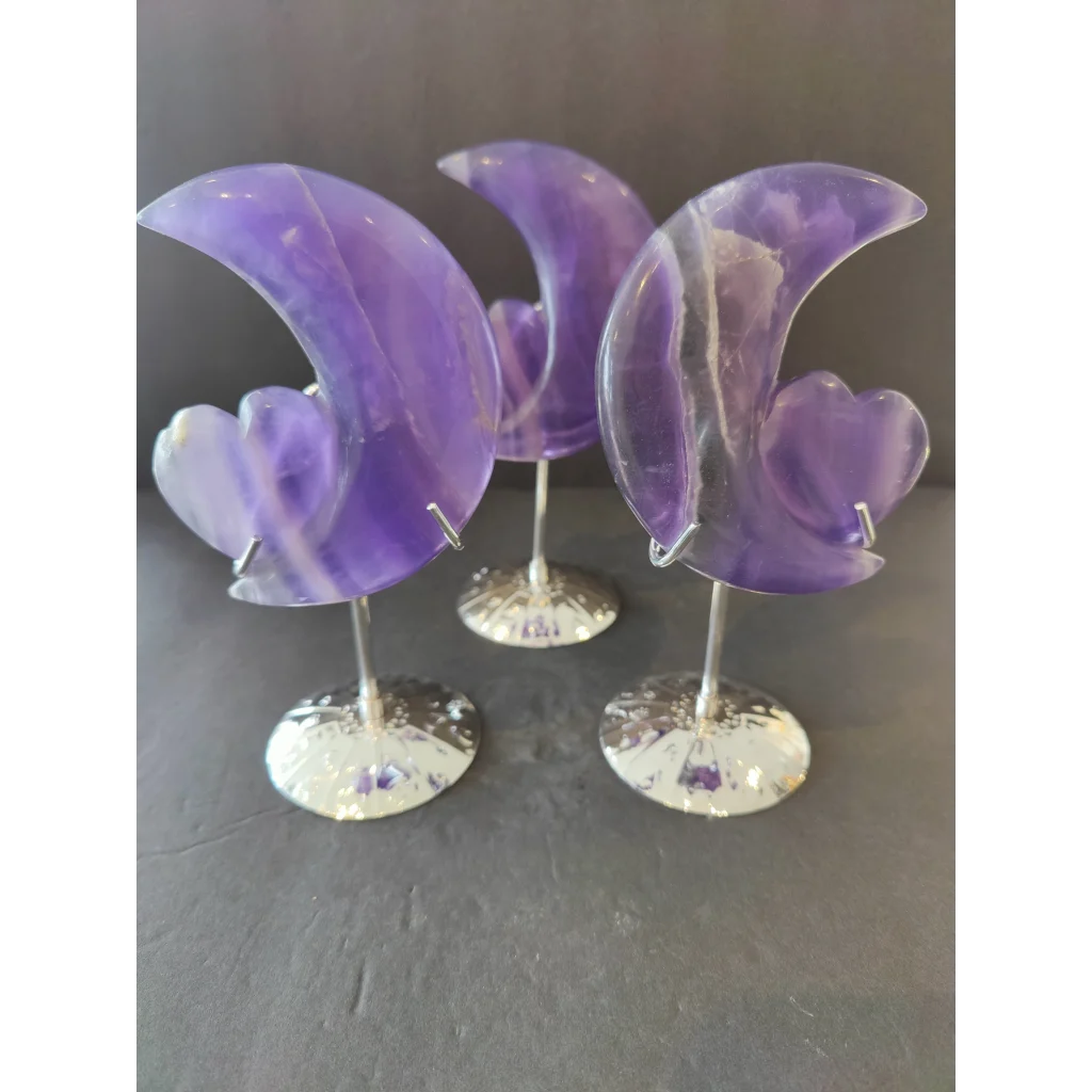 Three translucent purple fluorite half-moon heart sculptures on silver-toned metal stands for decorative display
