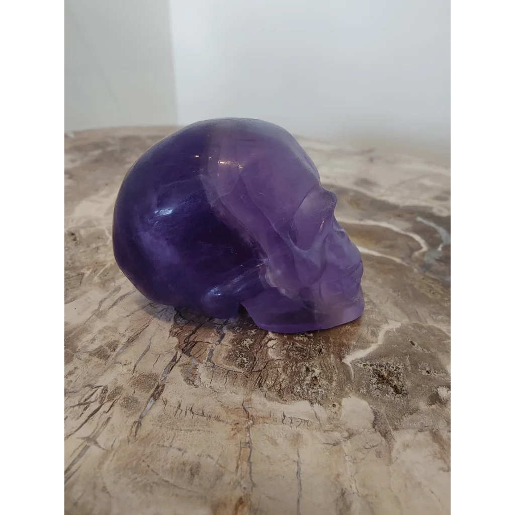 Purple fluorite skull sculpture with translucent polished surfaces and detailed facial features in amethyst hue