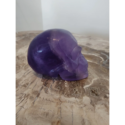 Purple fluorite skull sculpture with translucent polished surfaces and detailed facial features in amethyst hue