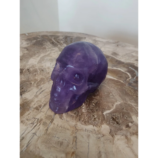 Purple fluorite skull sculpture featuring a translucent purple amethyst skull with polished surfaces and natural inclusions