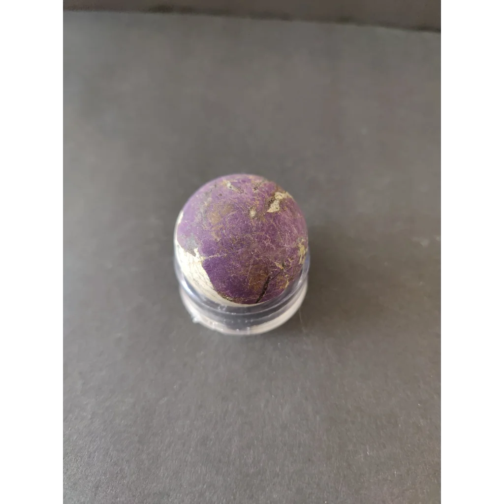 Purpurite lapidary specimen: round purple-white mineral with cracks in clear holder