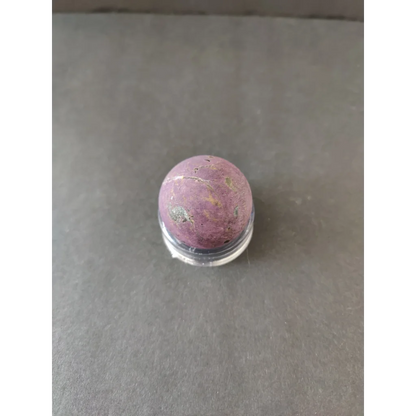Purpurite lapidary gemstone: smooth pinkish-purple round cabochon with golden gray inclusions on clear stand