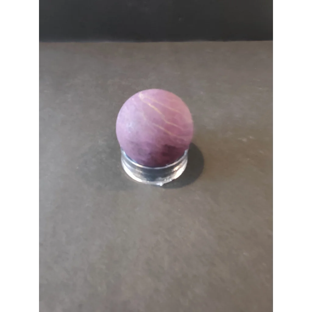 Purpurite Lapidary: smooth pinkish-purple stone with white veining on glass stand