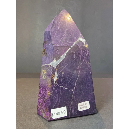 Purpurite polished obelisk tower sculpture in purple with white and gold veining standing upright on display surface