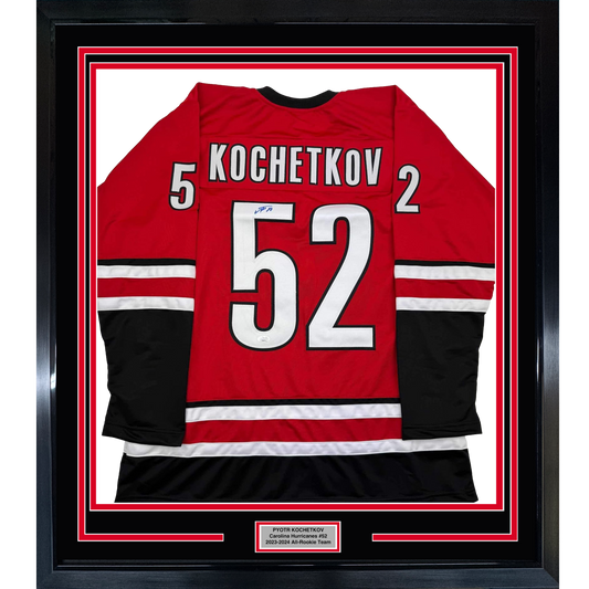 Framed red Carolina Hurricanes hockey jersey number 52 with "Kochetkov" nameplate, displayed flat against white background with black and red border matting.