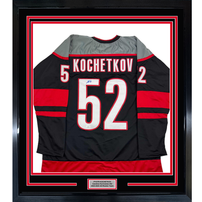 Framed black Carolina Hurricanes hockey jersey #52 with red stripes, displaying "KOCHETKOV" and number, mounted behind glass with red and white matting.