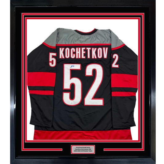 Framed black Carolina Hurricanes hockey jersey #52 with red stripes, displaying "KOCHETKOV" and number, mounted behind glass with red and white matting.
