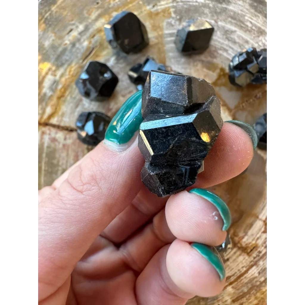 Hand holding rare melanite garnet from Kayes region, Mali, on wood