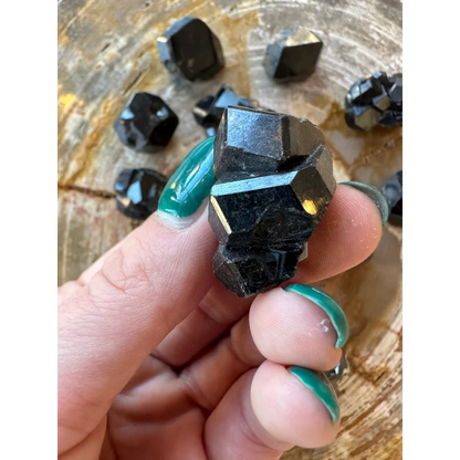 Hand holding rare melanite garnet from Kayes region, Mali, on wood