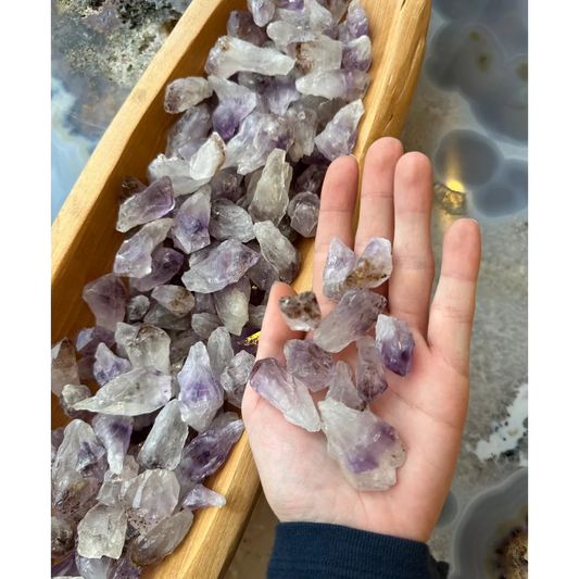Hand holding raw faceted amethyst crystals in wooden boat bowl on agate base