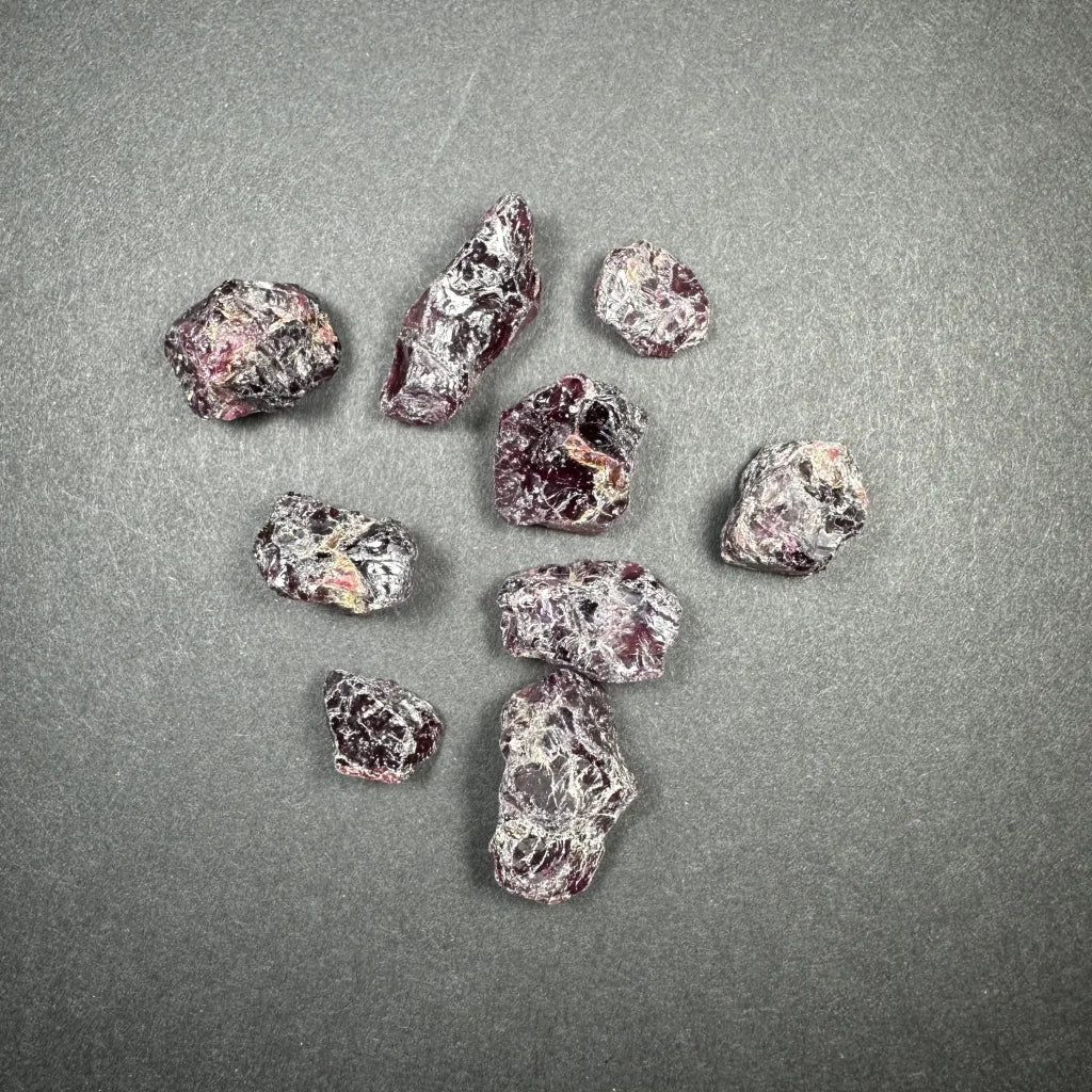 Raw garnet gemstones in deep red and purple hues on gray surface