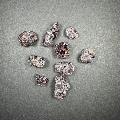 Raw garnet gemstones in deep red and purple hues on gray surface