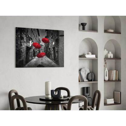 Black and white wall art of red umbrellas floating in cobblestone alley