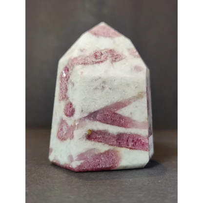 A polished pink and white rhodochrosite crystal geode quartz polished obelisk tower sculpture with a faceted pyramid top