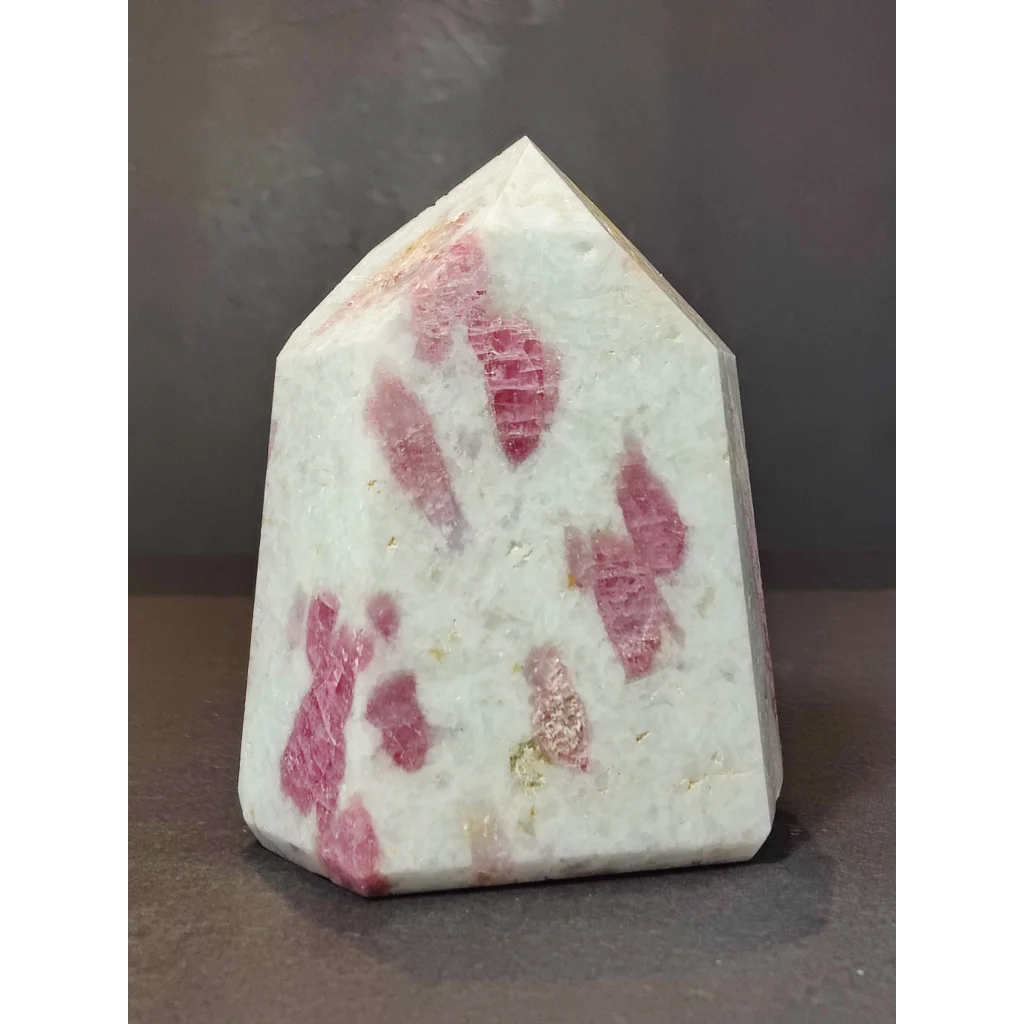 A polished white and pink rhodochrosite crystal quartz polished obelisk tower sculpture with a pointed house-shaped top